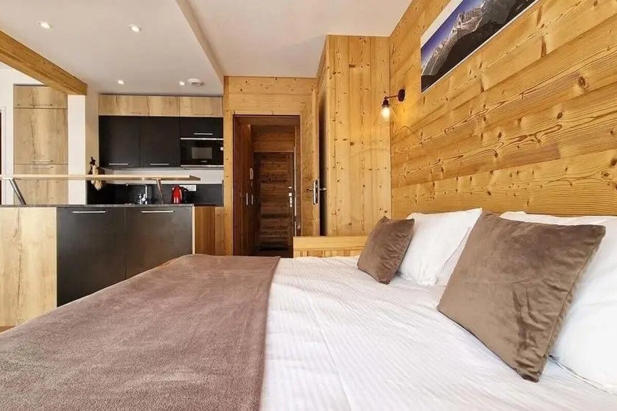 A bedroom with a bed and a kitchen in the background