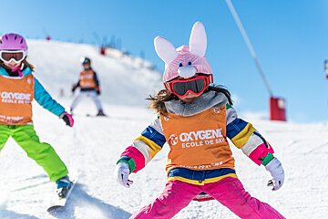 A little girl wearing an orange oxygene ecole de ski vest
