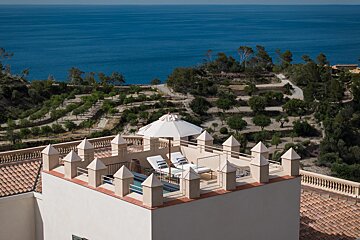 A balcony with a white umbrella overlooking the ocean