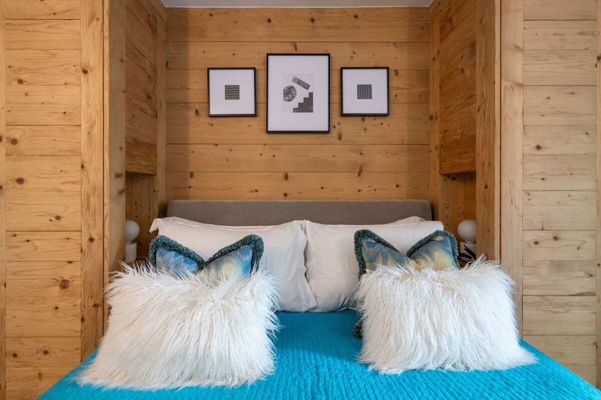 A bed with a blue blanket and white pillows against a wooden wall