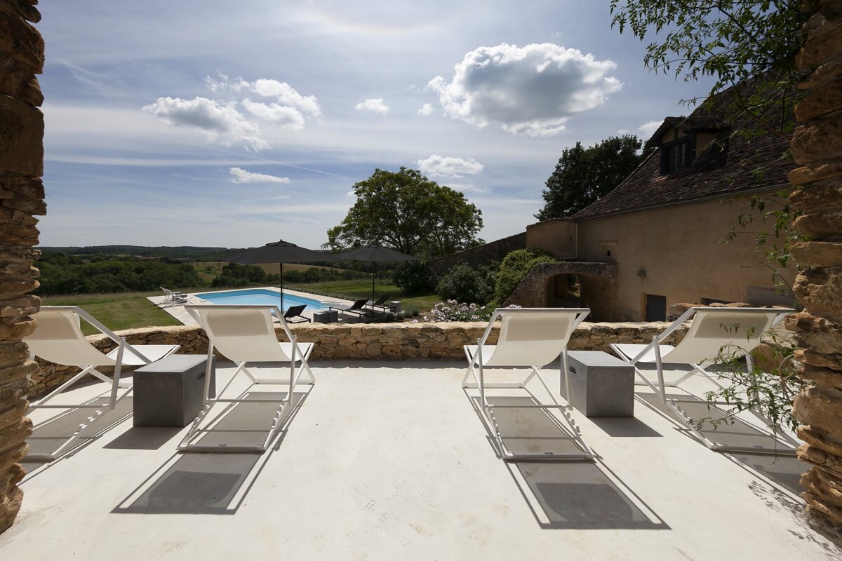 A patio with chairs and umbrellas overlooking a swimming pool