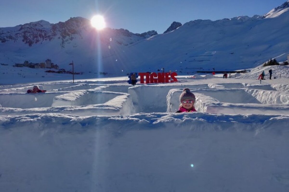 A child is playing in the snow near a sign that says tignes
