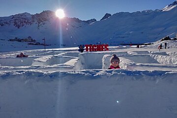 A child is playing in the snow near a sign that says tignes