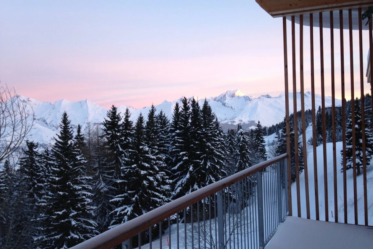 A balcony overlooking a snowy forest with mountains in the background