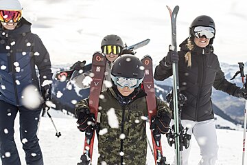 A person wearing a hh jacket is holding skis
