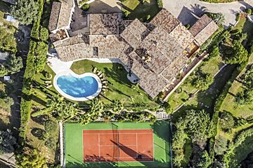 An aerial view of a tennis court in front of a large house