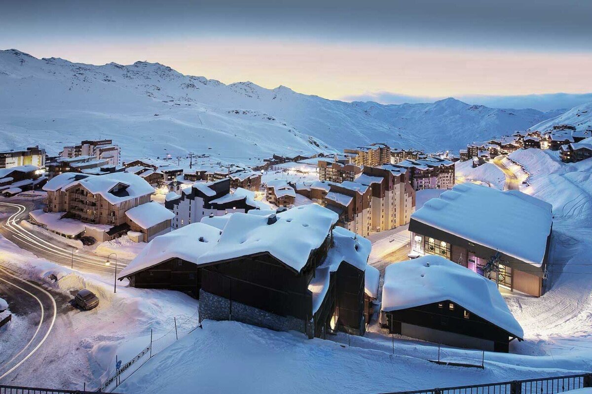 A snowy landscape with buildings and mountains in the background