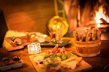 A wooden bucket filled with bread sits on a wooden table in front of a fireplace