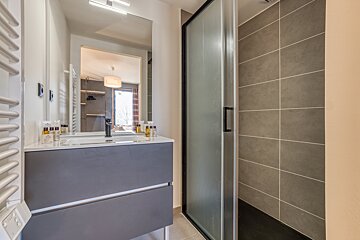 A modern bathroom featuring a gray vanity, a large mirror reflecting the room, and a walk-in shower with a frosted glass door.