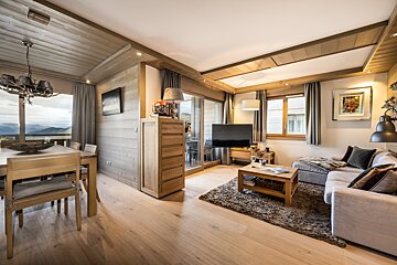 A warm, wood-clad open-plan living/dining room with stunning mountain views, cozy furniture, and modern lighting in a rustic-chic style.