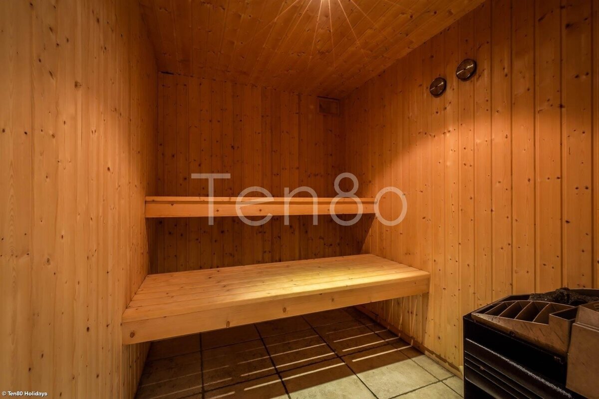 Interior of a cozy, light-wood sauna with two wooden benches, a sauna heater on the right, and tiled flooring.