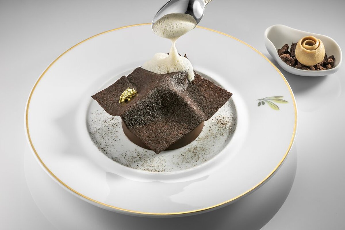 A white plate with a gold rim has a chocolate dessert on it