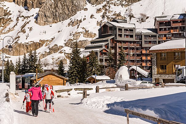 A group of skiers are walking down a snowy path in front of buildings