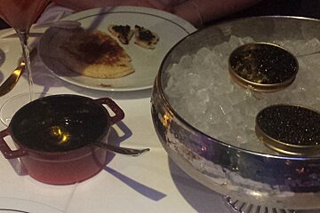 a table with caviar in an ice bucket and a bowl of sauce