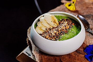 A bowl of green smoothie with bananas and granola on top