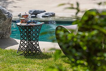 A table with a teapot and sunglasses on it in front of a pool