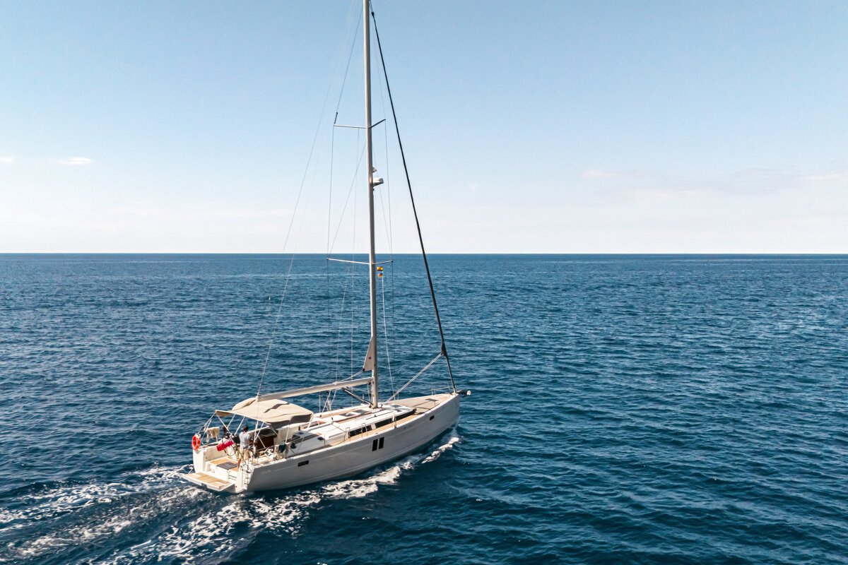 An aerial view of a white sailboat cruising through the deep blue sea under a clear sky.
