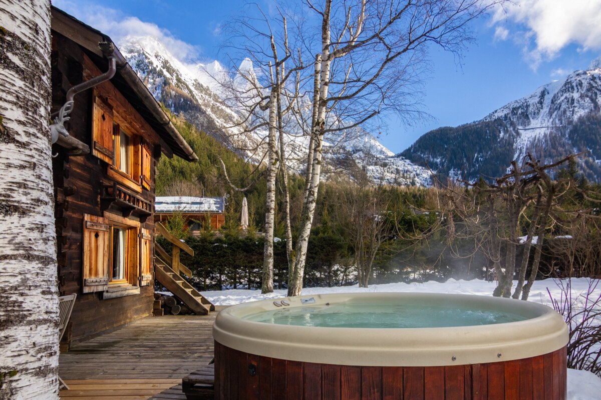 A hot tub sits on a deck in front of a snowy mountain
