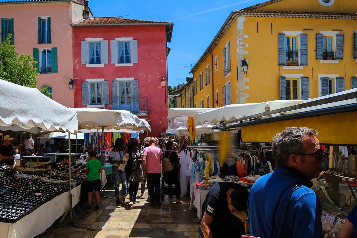 A group of people are shopping at a market with a pink building in the background