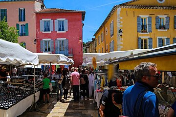 A group of people are shopping at a market with a pink building in the background
