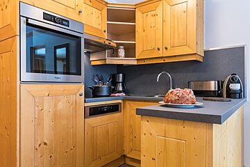 A cozy kitchen with light wooden cabinets, a built-in stainless steel oven, dark countertops, a sink, coffee maker, and a festive cake.