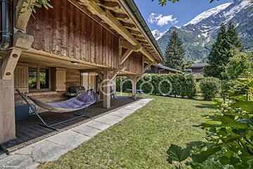 A hammock sits on a patio in front of a wooden house