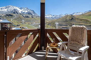 A chair with a knitted blanket on it sits on a balcony overlooking mountains