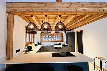 A modern kitchen with natural wood beams and ceiling, dark gray cabinets, a light island, and three woven pendant lights.