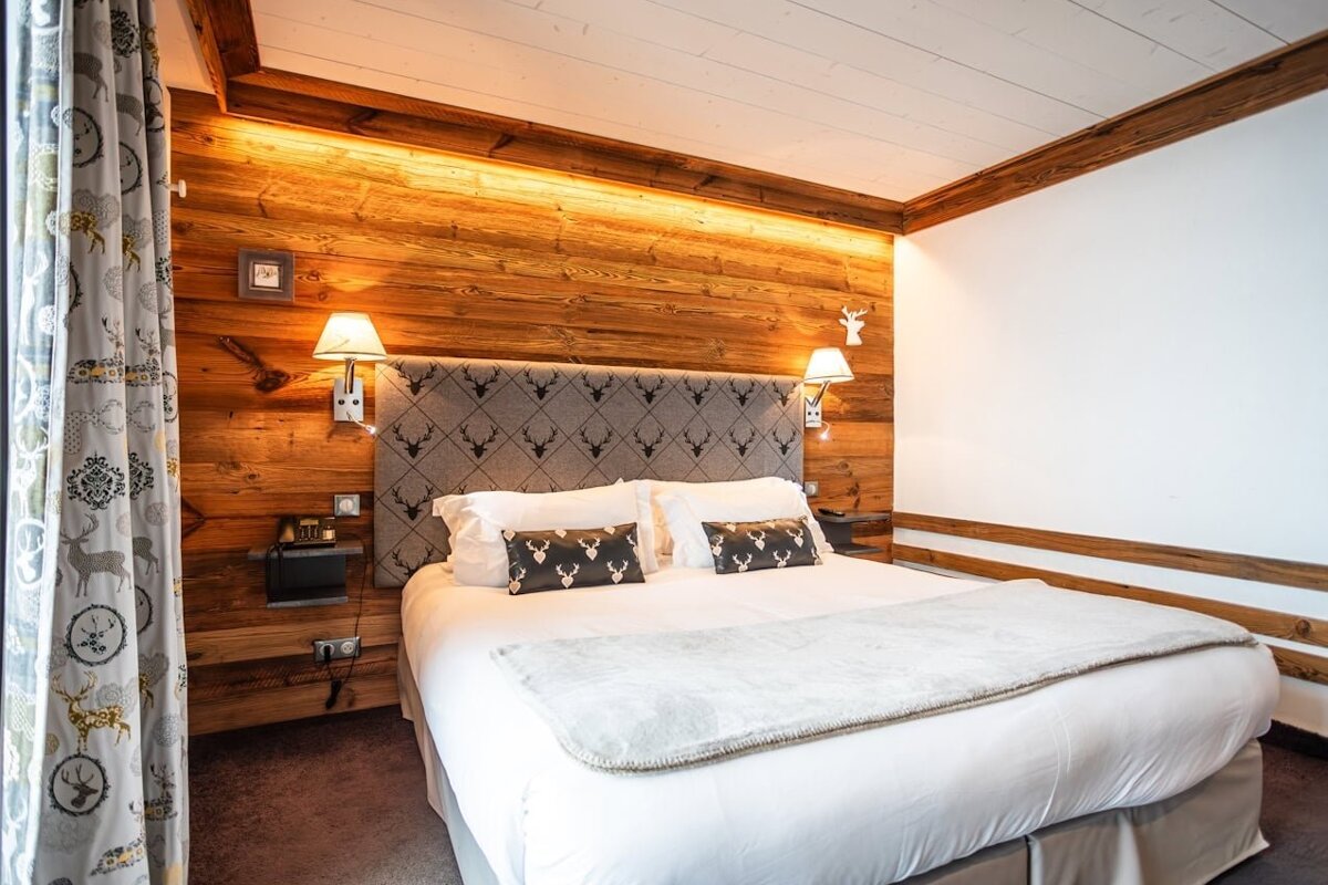 Cozy, wood-paneled bedroom with a fur-covered bed, robes, and a stunning view of snowy mountains from a balcony. Perfect winter retreat.