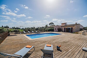 A large swimming pool is surrounded by chairs and umbrellas on a wooden deck