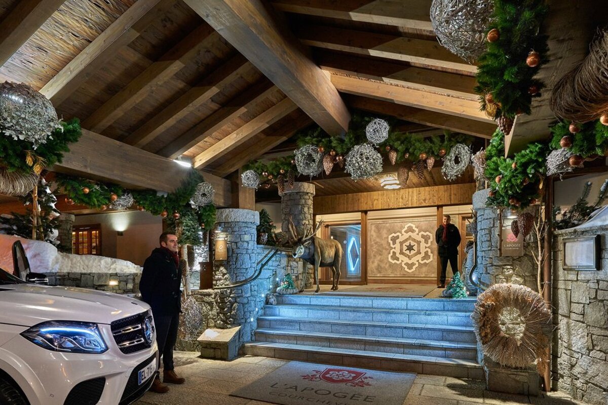 A white mercedes is parked in front of a building that says l' apogee