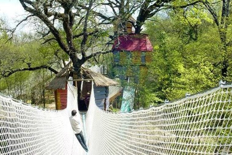 A man is walking across a rope bridge to a tree house