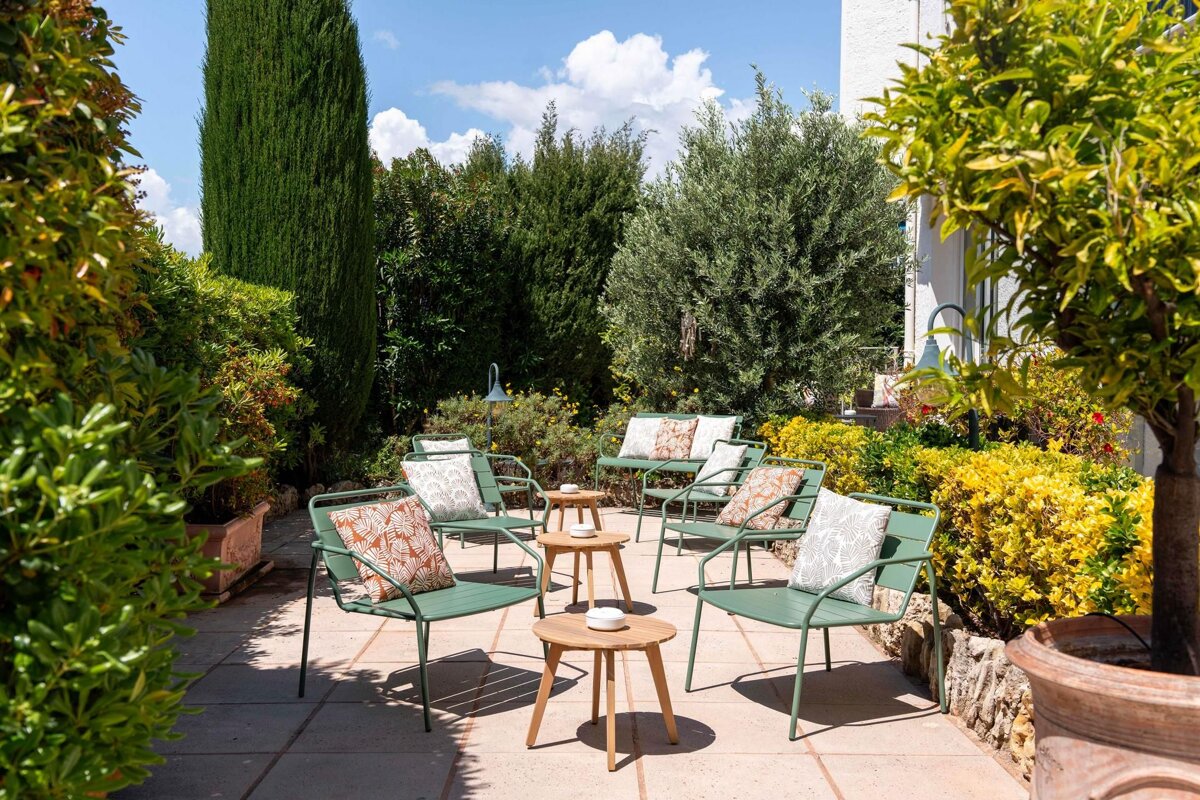 A patio with green chairs and tables with pillows on them
