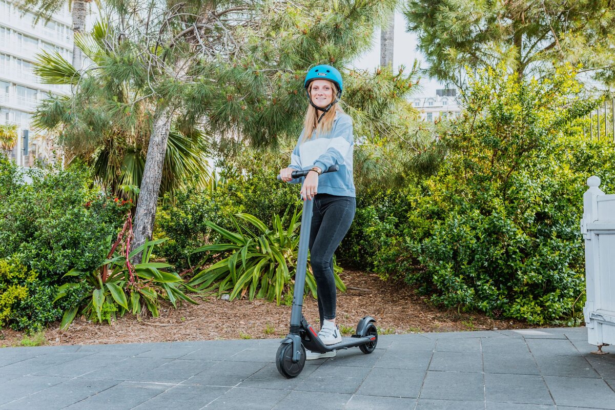 A woman wearing a blue helmet is riding an electric scooter