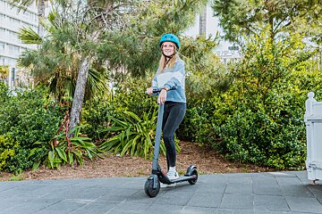 A woman wearing a blue helmet is riding an electric scooter