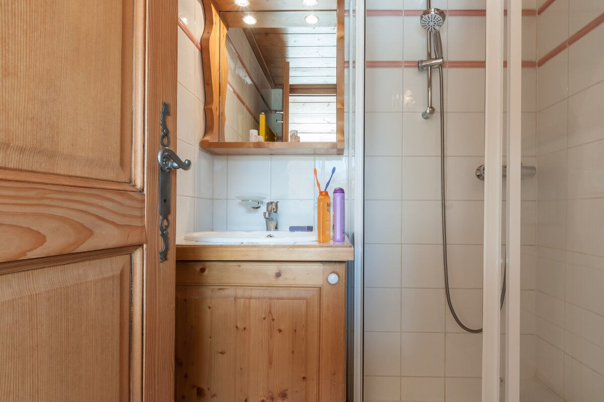 A bathroom with a sink and a shower with a bottle of shampoo on the counter