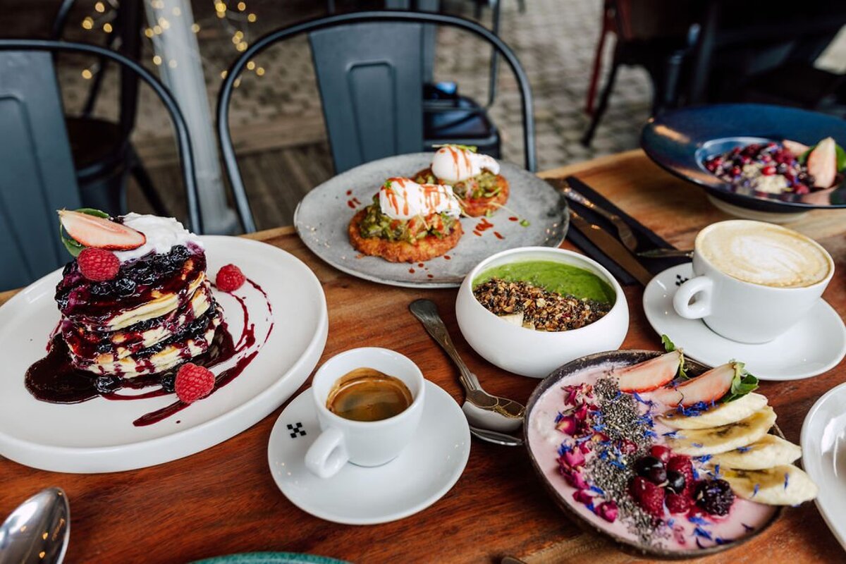 A table topped with plates of food including pancakes and smoothies