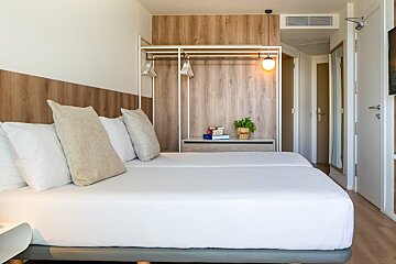 A modern hotel room with twin beds, white bedding, wood accents, an open closet, and a small shelf with a plant.