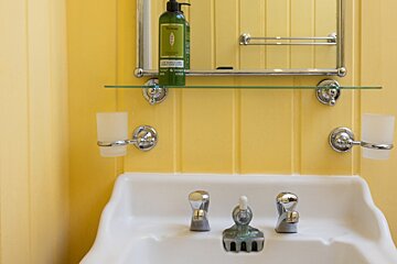 A bathroom sink with a bottle of verveine on the shelf