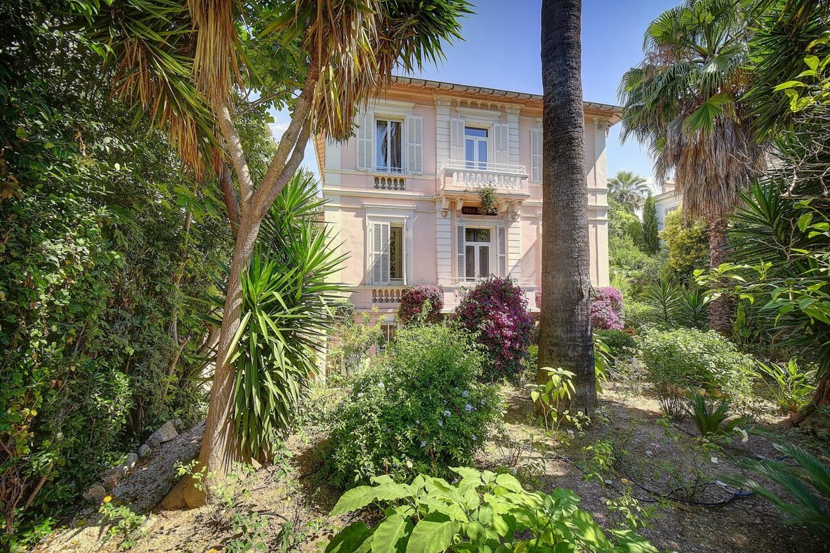 A pink house is surrounded by palm trees and bushes