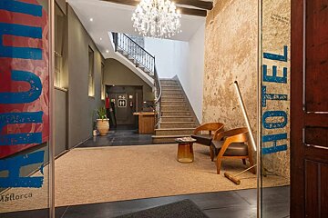An inviting hotel lobby entrance with a grand staircase, crystal chandelier, seating area, rustic wall, and 