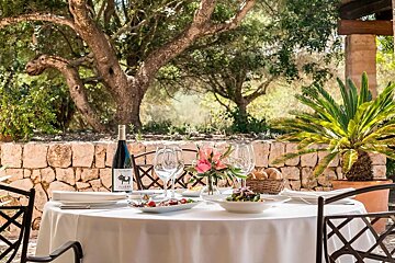 An elegant outdoor dining table with wine, salads, and bread, set against a rustic stone wall and lush trees.
