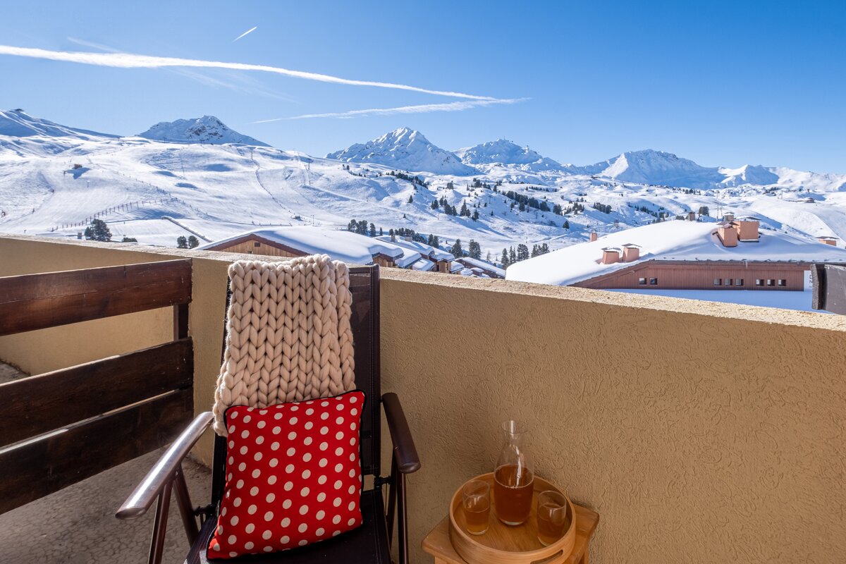 A chair with a polka dot pillow sits on a balcony overlooking snowy mountains