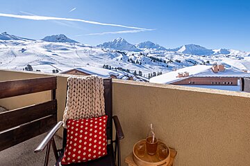 A chair with a polka dot pillow sits on a balcony overlooking snowy mountains