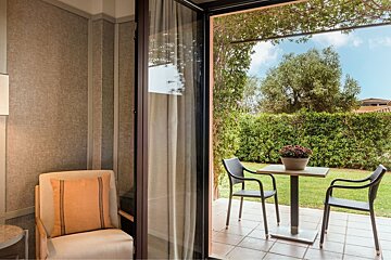 Cozy indoor space overlooking a patio with a table and chairs, leading to a vibrant green garden under a sunny sky.
