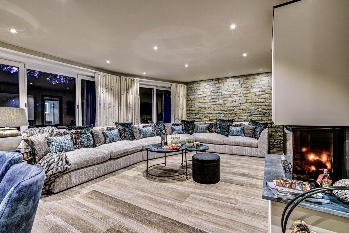 Luxurious living room with a large sectional sofa, inviting fireplace, stone accent wall, large windows, and modern decor.