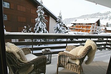 Two wicker chairs on a balcony overlooking snow covered trees