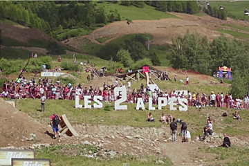 A large group of people are gathered around a sign that says les 2 alpes