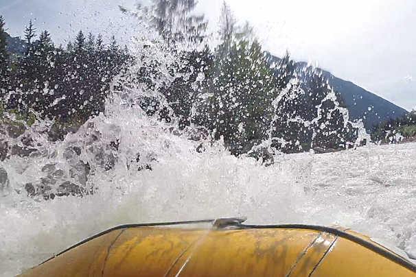 A yellow raft is going down a river with a mountain in the background