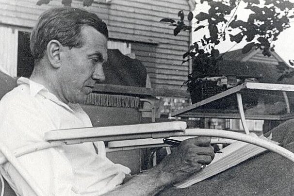 a black & white photo of a man writing in a sun chair
